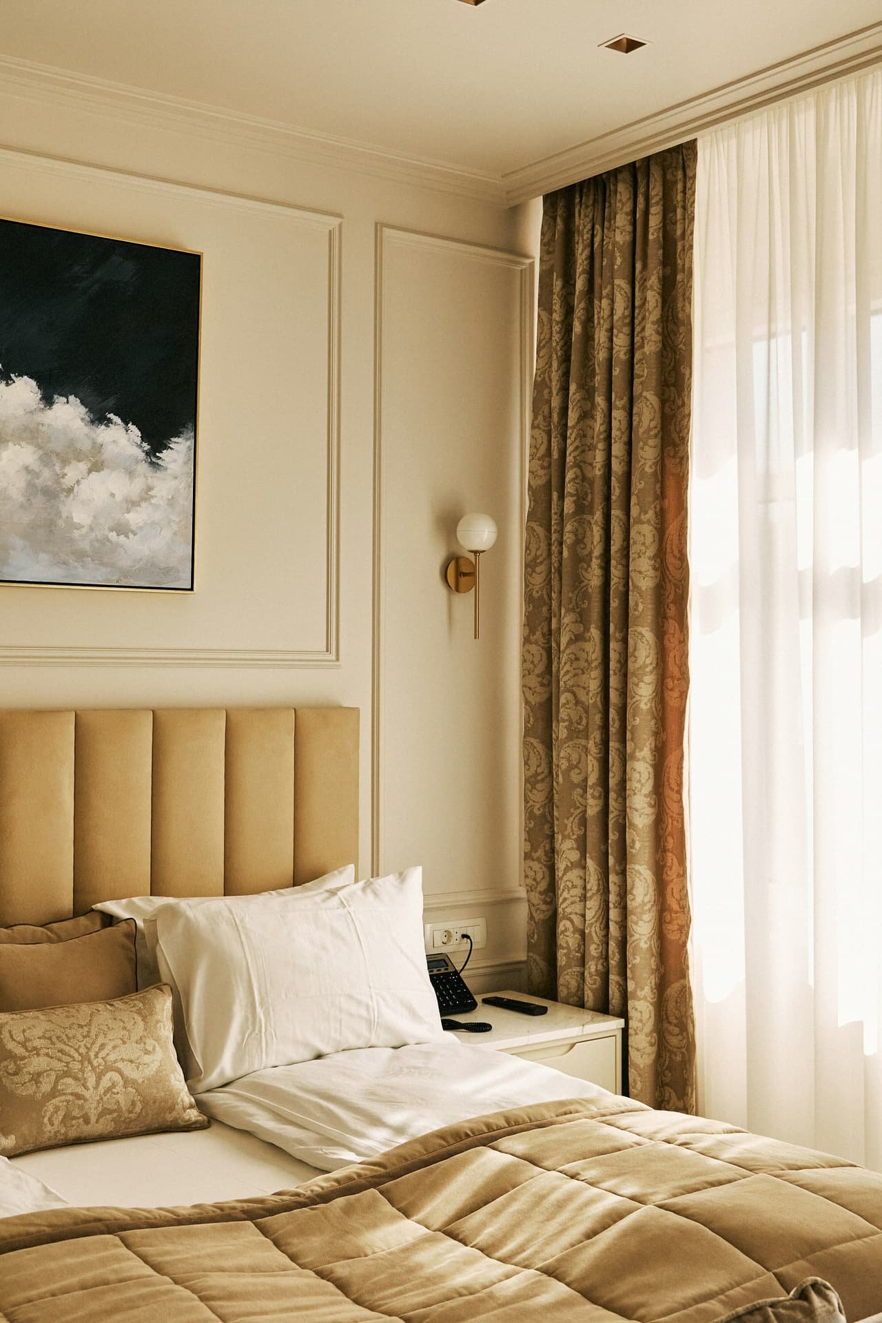A quiet bed with a padded headboard, a wall lamp and long curtains