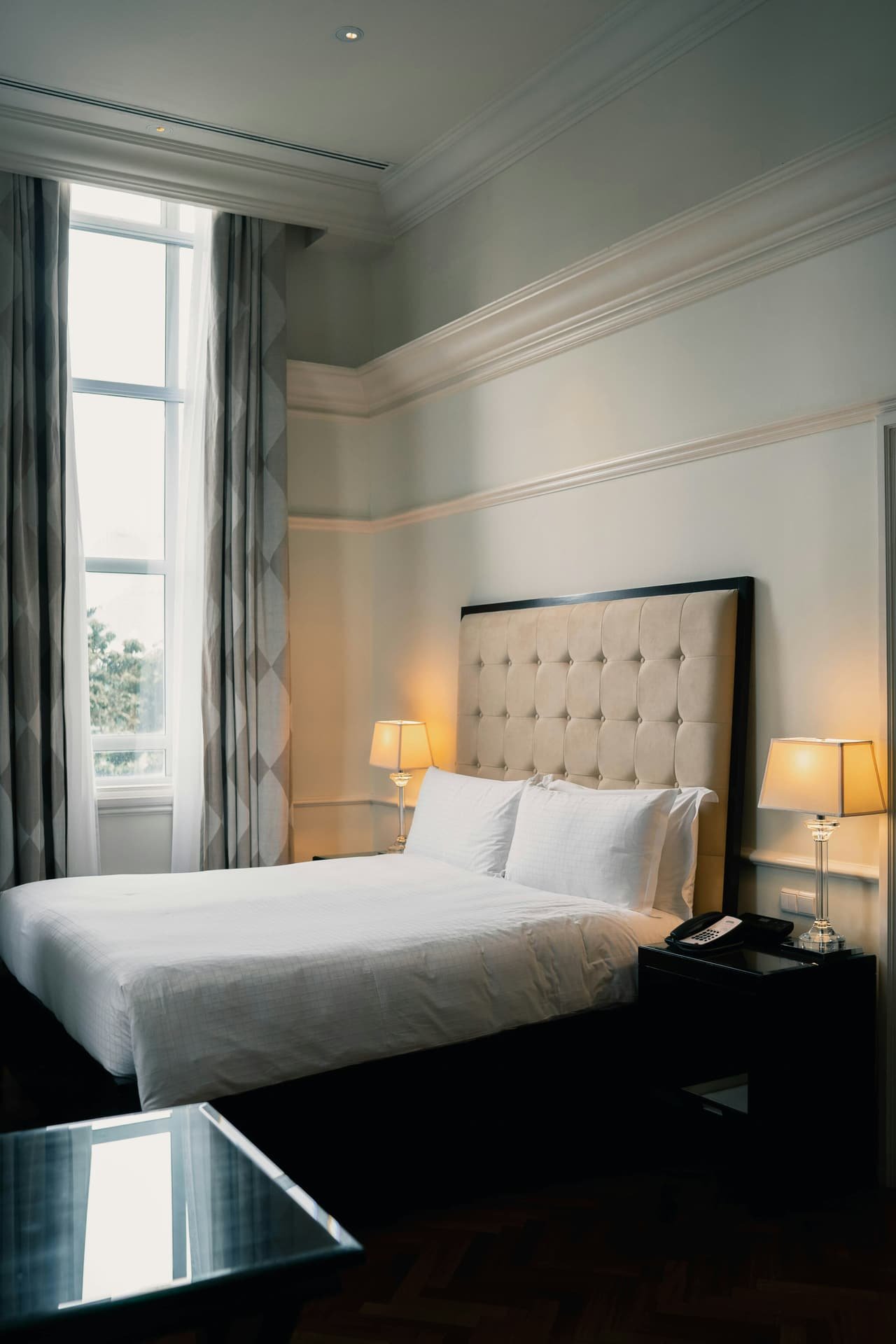 A made bed with a tall padded headboard and two lamps